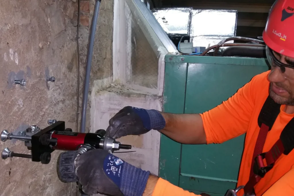 Trabajador con casco y arnés instalando un anclaje en una pared