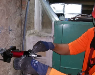 Trabajador con casco y arnés instalando un anclaje en una pared